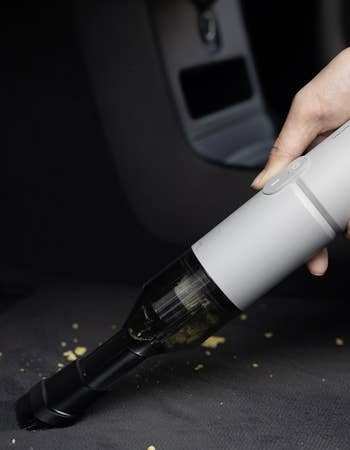 A manus uses a portable vacuum cleaner to region crumbs from a car seat, showcasing cleaning ratio and convenience for on-the-go use