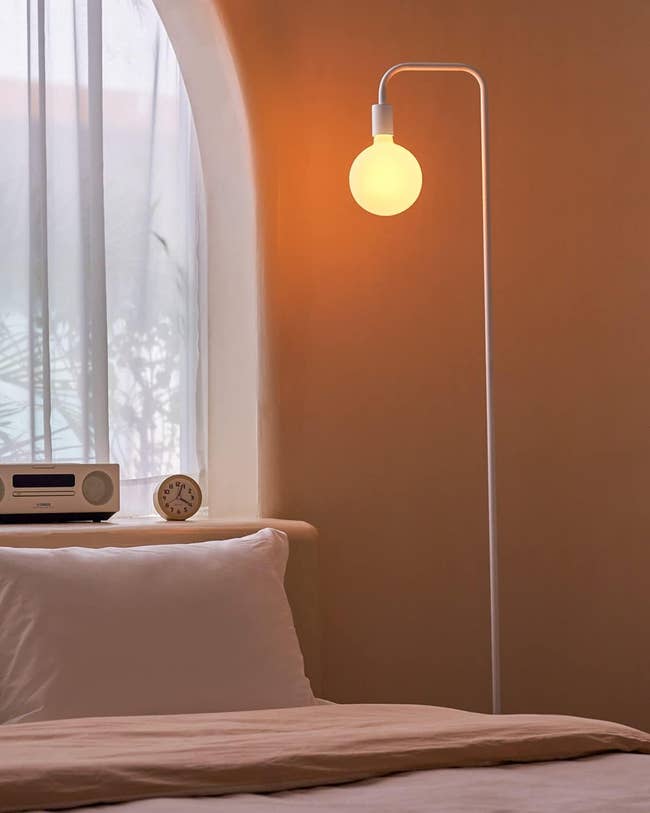 Floor lamp with a simple design next to a bed, ideal for a minimalist bedroom decor