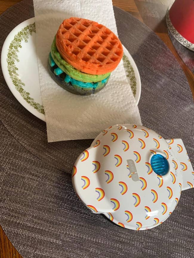 reviewers white and rainbow waffle maker next to plate of colorful waffles