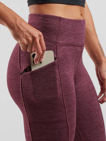 Model putting phone into side pocket of maroon heathered leggings 