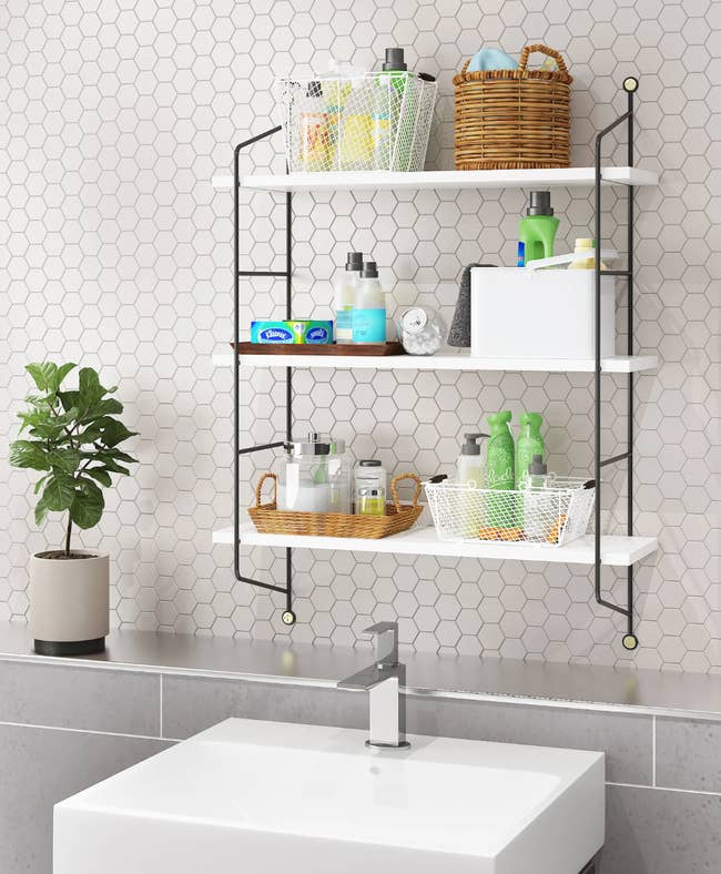 White and black metal three-piece shelf with baskets and toiletries hanging over a white sink