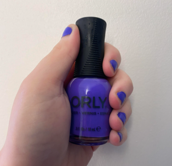 buzzfeed editor wearing and holding the bottle of vibrant purple nail polish