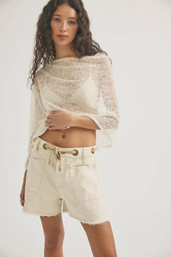 A person wearing a sheer top and high-waisted shorts poses, showcasing a casual summer outfit