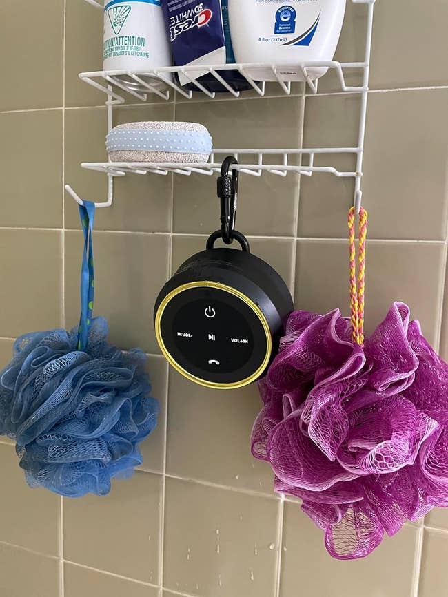 Waterproof speaker hanging from a shower caddy next to hygiene products and loofahs