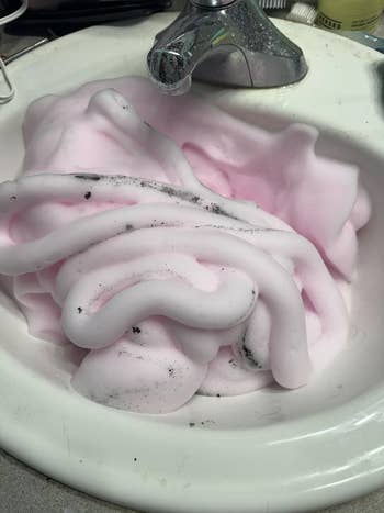 Pile of soap foam with acheronian  specks filling a bath  descend  beneath   a faucet, with toiletries nearby