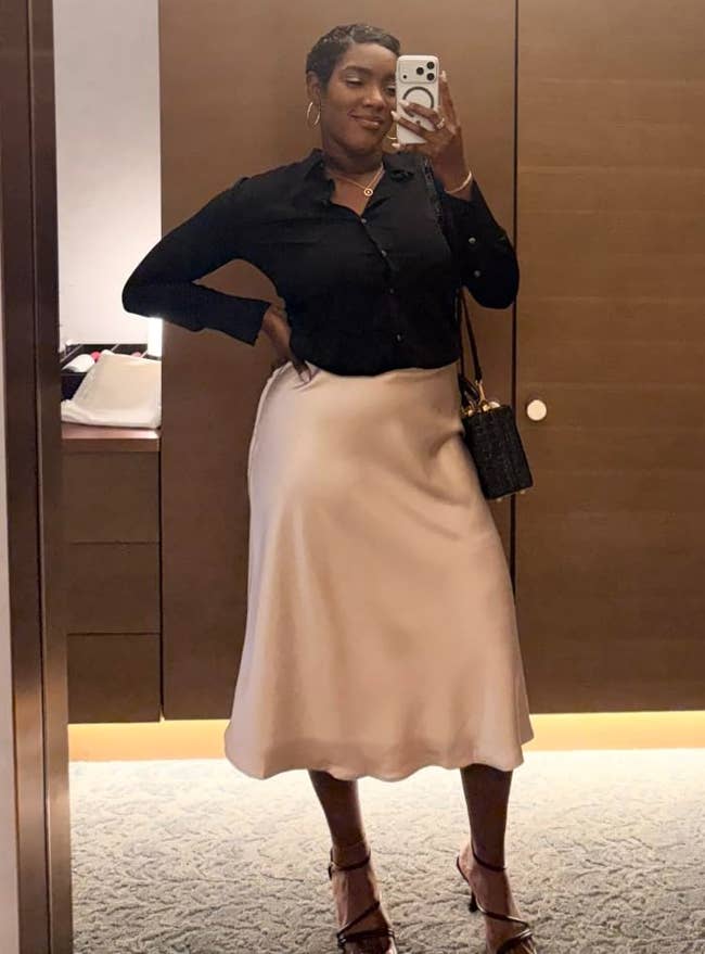 Person taking a reflector selfie, wearing a stylish achromatic blouse and airy skirt, accessorized with a tiny handbag