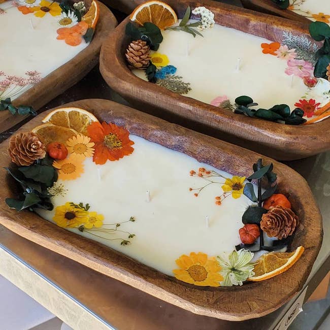 Two wooden dough bowls with white candle wax and natural flowers and pinecones inside on a tray