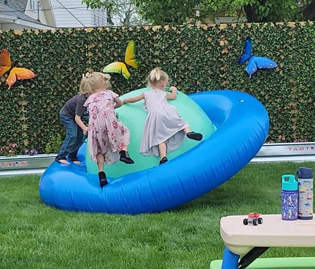 Three children playing on a large inflated saturn toy in a backyard