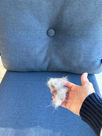 Hand holding a clump of favored  fur implicit    a cloth  chair