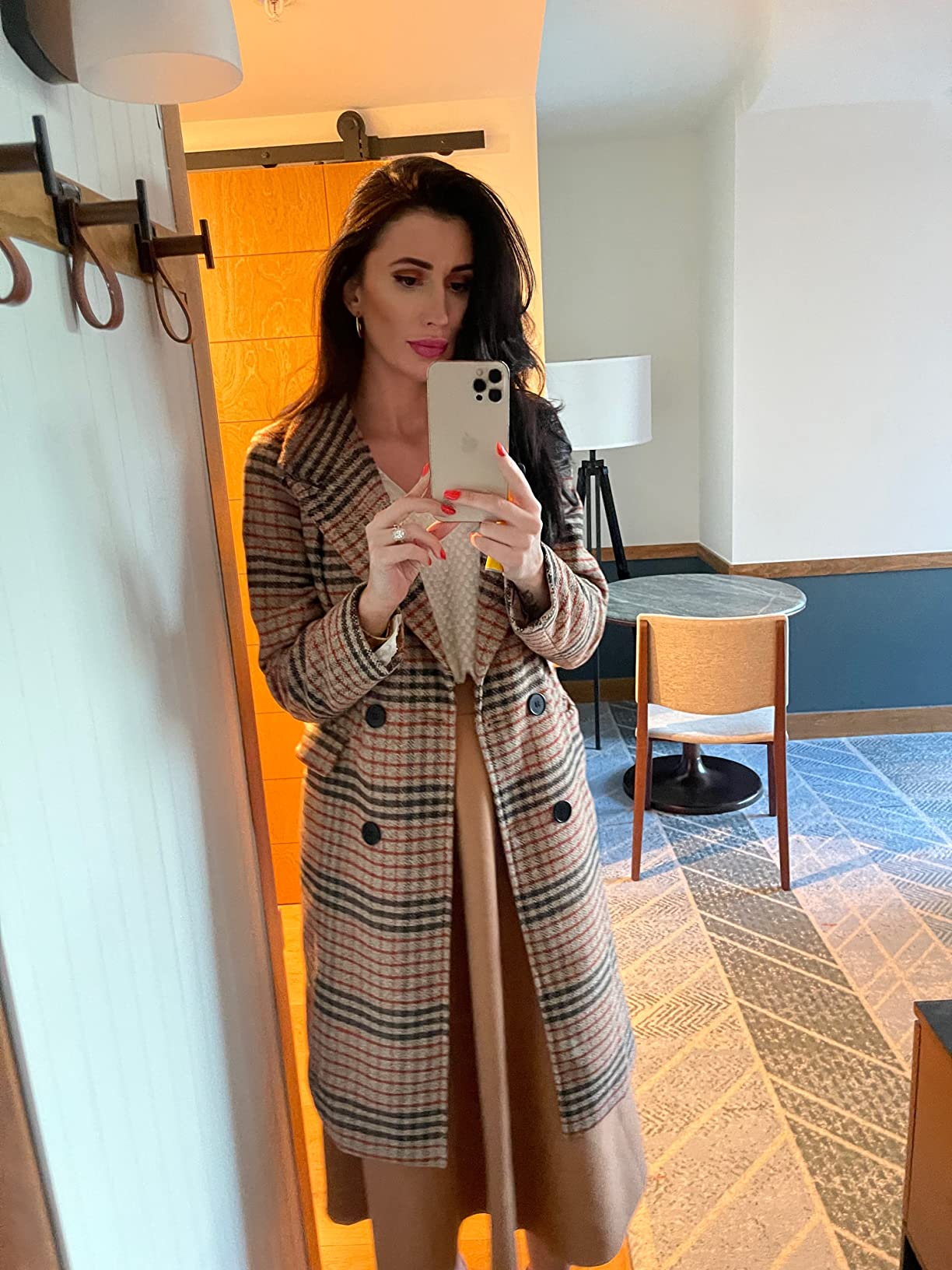 Person taking a reflector  selfie successful  a stylish plaid double-breasted overgarment  implicit    a agelong  dress, lasting  successful  a modern, minimalistic room