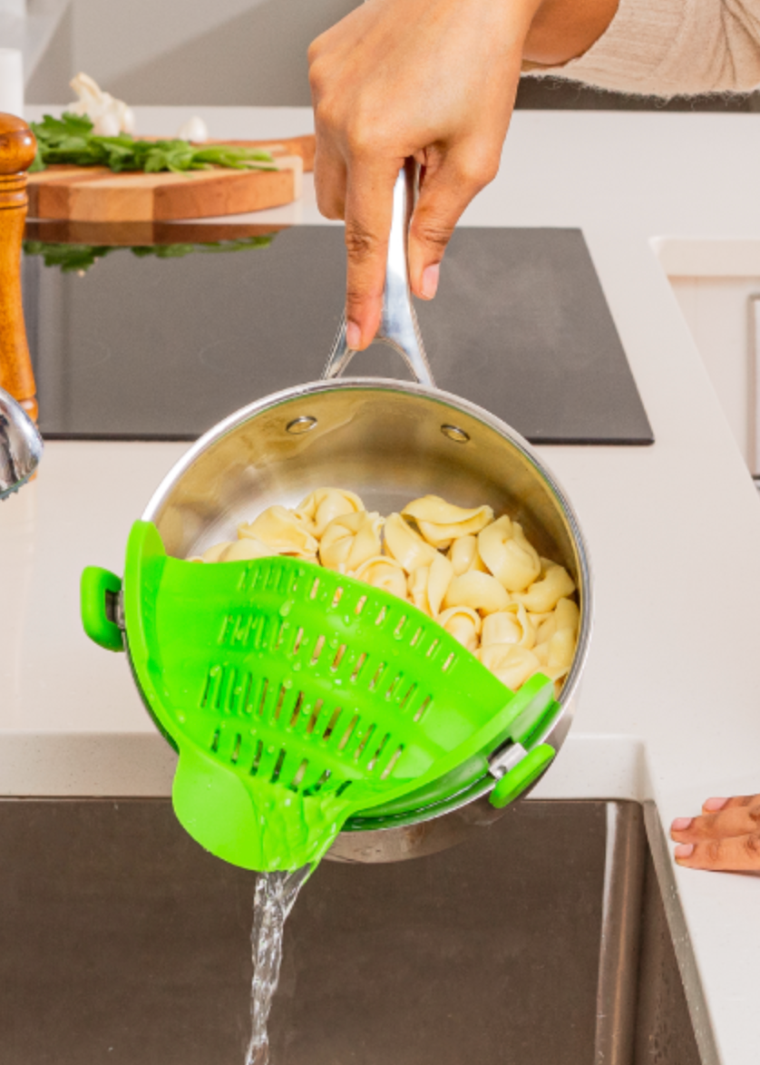 A model straining pasta from a green strainer clipped to the sides of the pot 