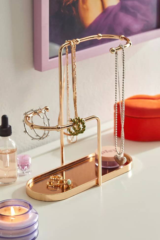 Jewelry stand with necklaces and bracelets on a dresser beside a candle, ideal for organizing accessories