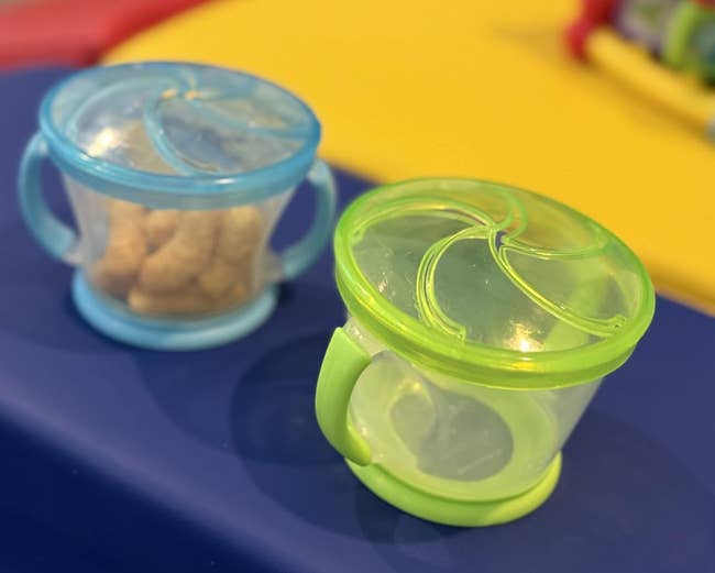Two snack containers with lids connected a table. One contains tiny snacks, portion the different is empty. Perfect for on-the-go snacking