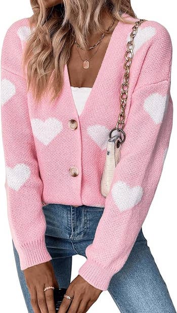 Person wearing a pink heart-patterned cardigan and jeans, with a chain strap purse