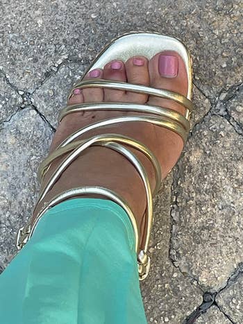 Close-up of a ft  wearing a metallic strappy sandal paired with teal pants, lasting  connected  a textured chromatic  surface