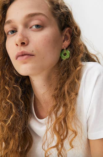 a model wearing gold hoops with green flower charms