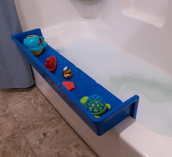 A bathtub filled with bubbles and a blue topper on top that is holding a child's bath toys