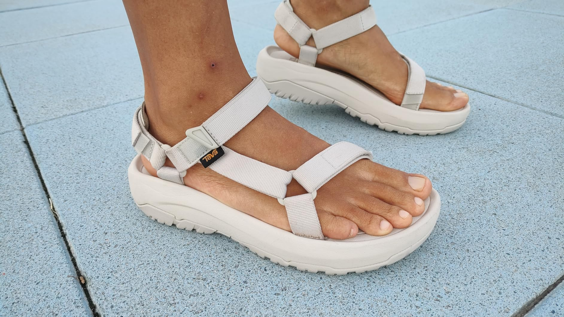Person wearing level    sandals with heavy   soles and adjustable straps, lasting  connected  a tiled surface