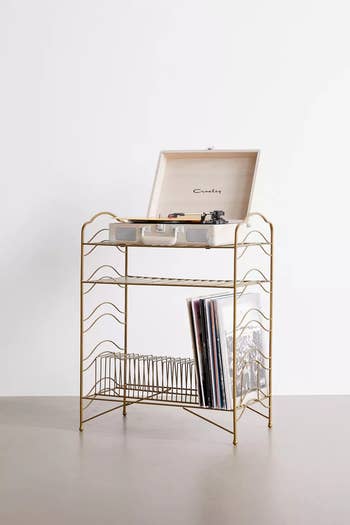 A gold wire vintage style storage rack with a record player on top and vinyls on the bottom shelf 