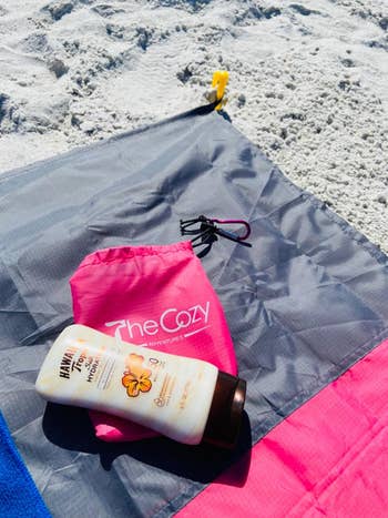 reviewer photo of blanket on the beach, and pink carrying bag and sunscreen