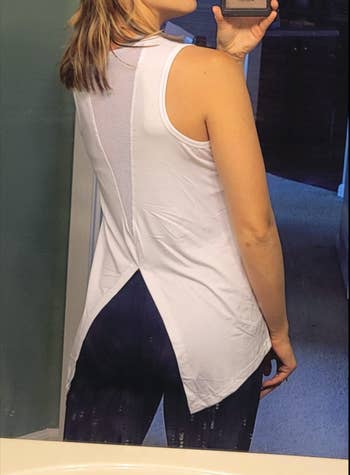 Reviewer showing the back of a white tank with a V-shaped mesh cut out and side flaps of fabric over the hips 