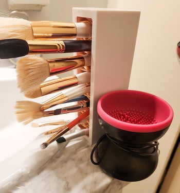 The tool next to a container with a reviewer's brushes drying out, showing the silicone bristles on the bottom of the spinning bowl