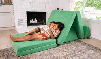 Two children smiling and lounging connected a foldable greenish play sofa successful a cozy surviving room, adjacent a fireplace