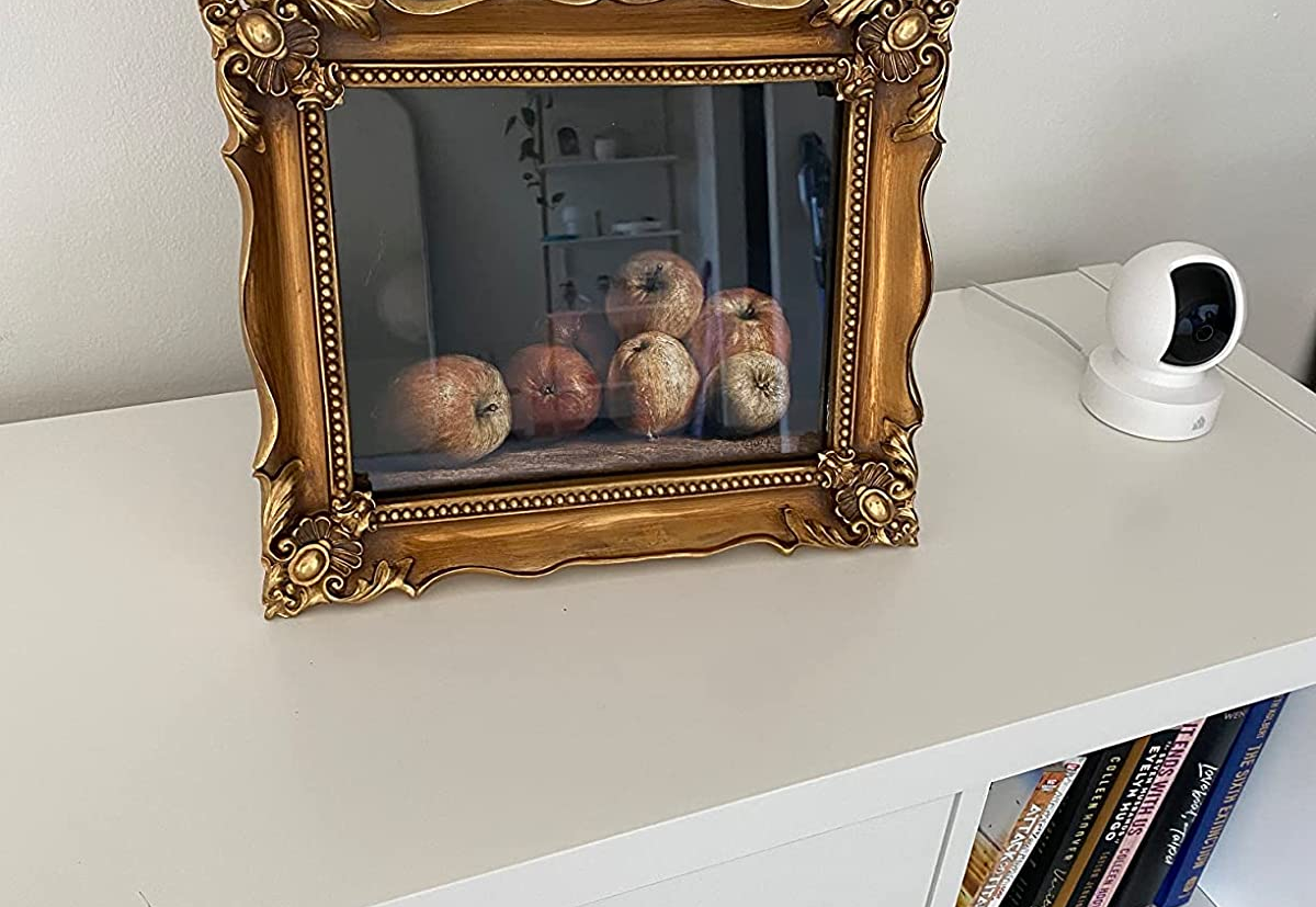 Reviewer image of gold antique-inspired frame with photo of fruit on top of white dresser next to camera