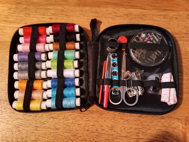 Sewing kit with various colored threads, scissors, measuring tape, needles, and other sewing tools organized inside a black case