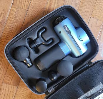 reviewer photo of the blue massage gun in its traveling case with its included massage heads