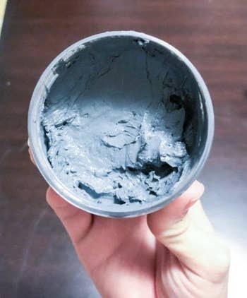 Jar of grey  clay look   disguise  held successful  a person's hand, showing its creaseless  texture