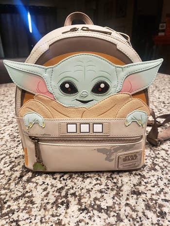 A mini back pack with baby yoda on the back and his ears sticking out