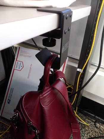 A red handbag leaning hanging from a clamp mounted on a white desk