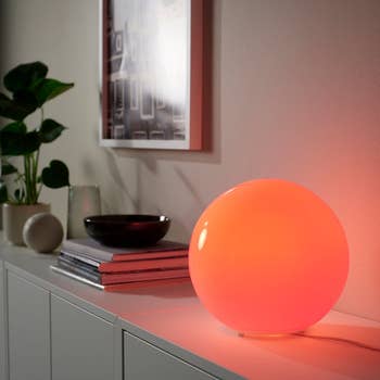 A modern, spherical lamp casting a warm glow on a white cabinet with books and decor, enhancing a stylish home setting