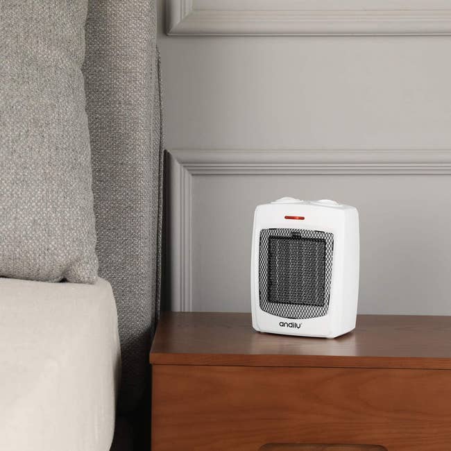 Compact white space heater on a wooden table beside a sofa, suitable for home use