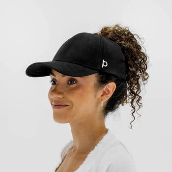 Model with curly high ponytail pulled through the magnetic hole in the back of the hat 