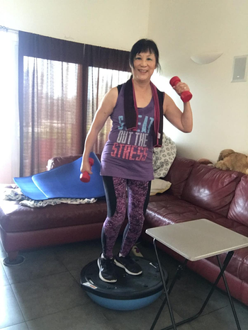 reviewer wearing one of the cooling towels around their neck while exercising in their living room
