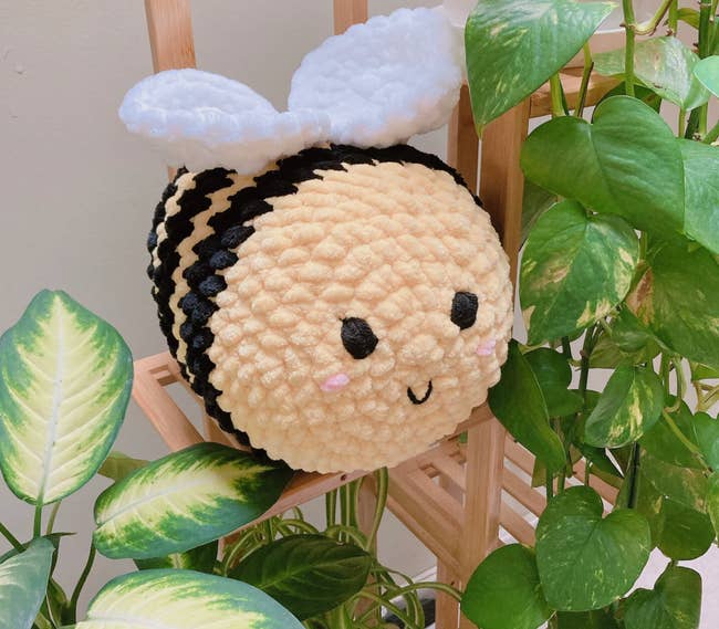 A crocheted yellow bee with black stripes sitting on a planter