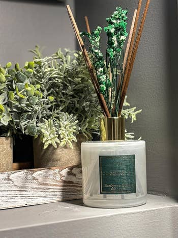Aromatic diffuser with sticks on a shelf beside artificial greenery