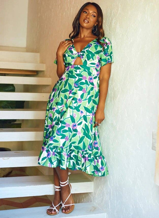 model wearing a short-sleeve midi dress with a knotted front and a green floral pattern with purple and blue orchids