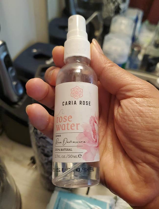 A hand holds a bottle of rose water spray