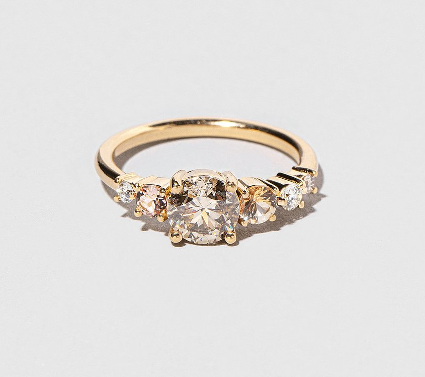 a ring with five stones, four small peach and clear stones with one champagne larger stone in the middle set on a gold band