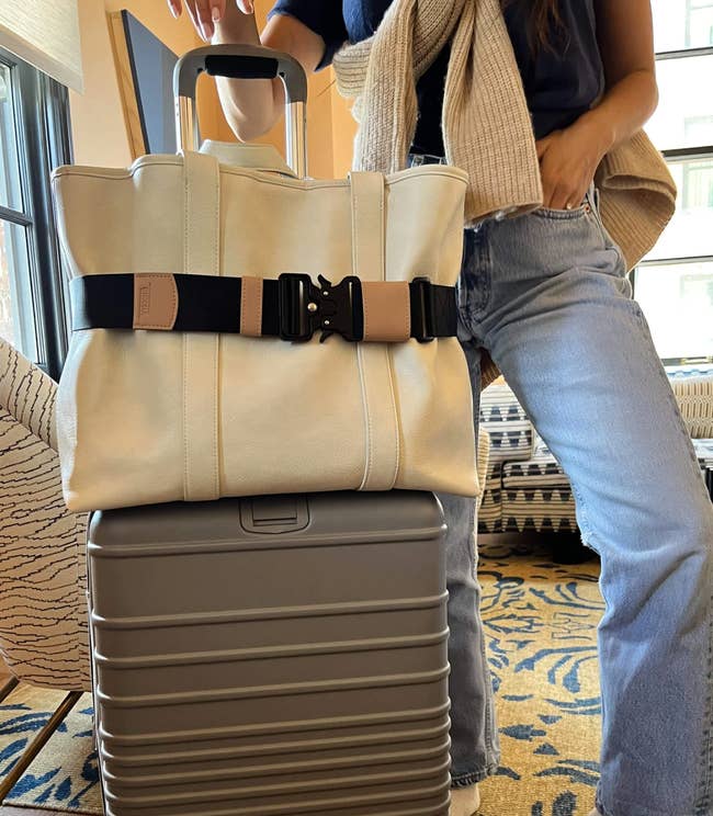 Model using the travel belt to hold a carry on bag on top of a rolling suitcase