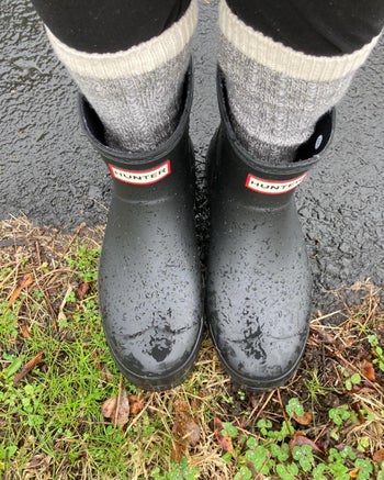 a reviewer wearing dark gray hunter boots in the rain