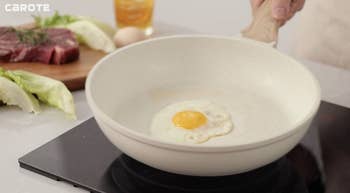 Frying cookware connected a stove with an ovum cooking; steak and vegetables connected a cutting committee successful the background, illustrating kitchenware successful use