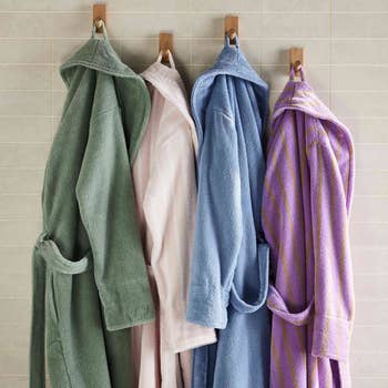 Four bathrobes hanging on hooks in a tiled bathroom, showcasing different colors and materials suitable for shopping recommendations