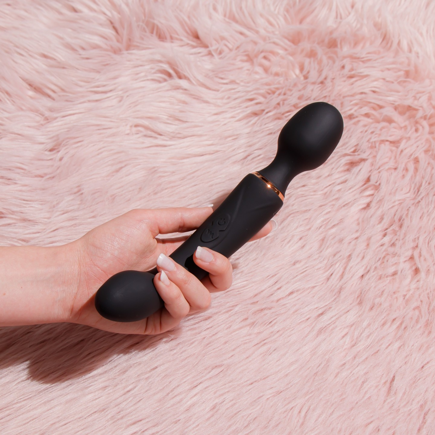 Model holding black wand vibrator on plush pink background
