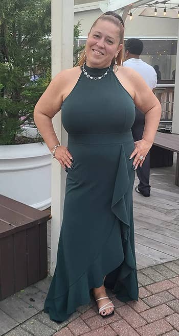 Reviewer wearing dark green halter maxi dress with ruffle side slit and bottom with a necklace and strappy heels