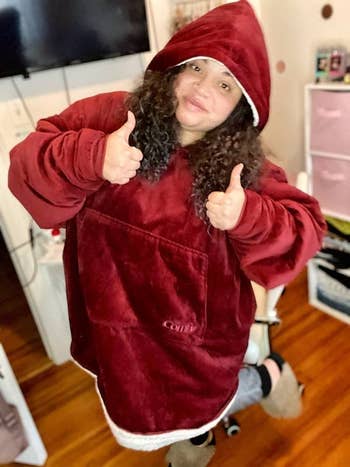 Person wearing an oversized hooded fleece sweatshirt giving thumbs up   successful  a cozy room