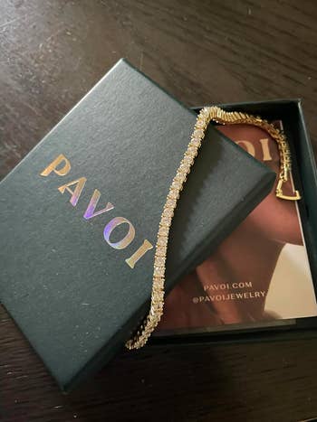 Pavoi branded jewelry box with a finely crafted gold bracelet resting on it. 